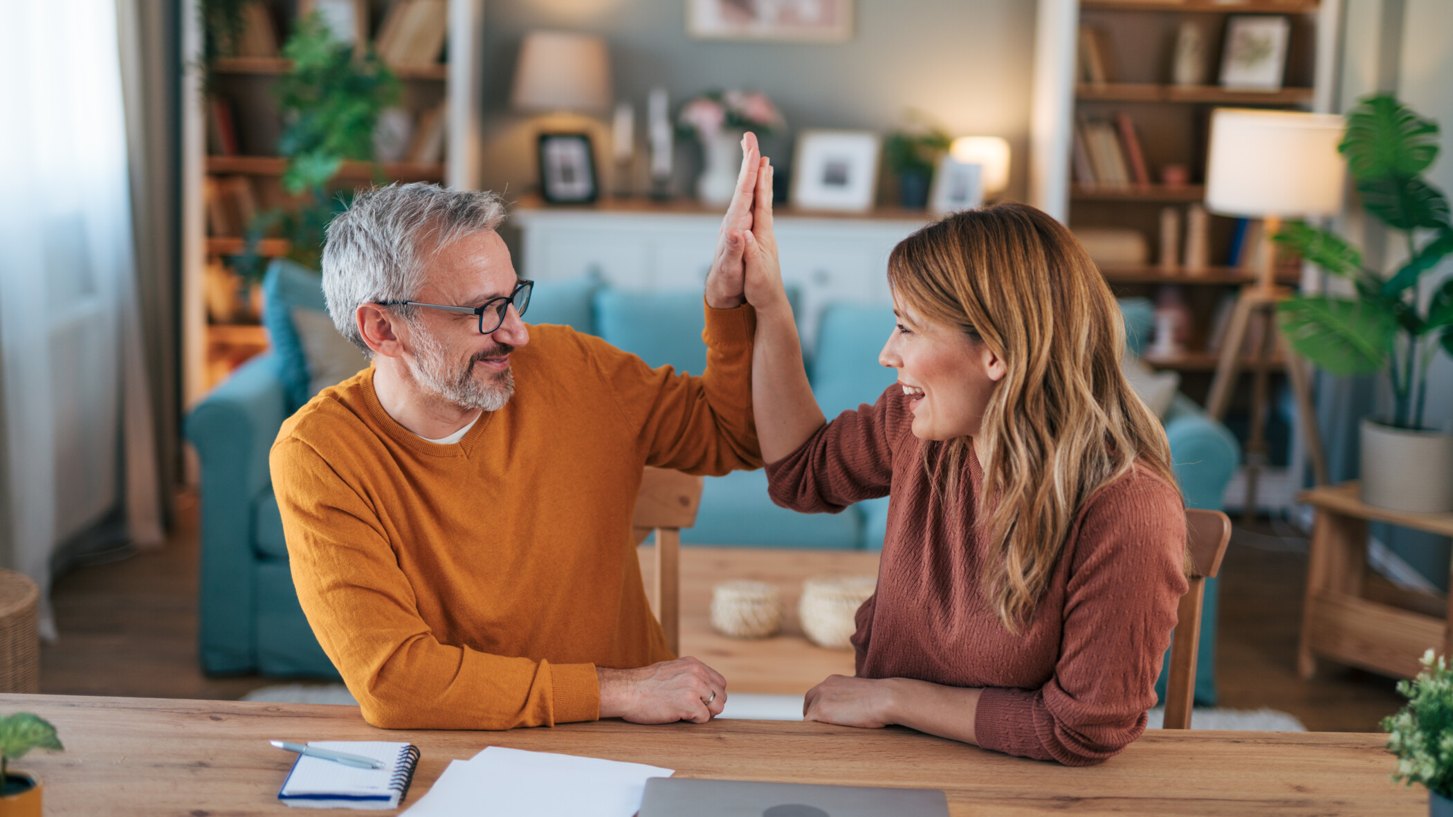 Pärchen sitzt zuhause am Esstisch und macht lächelnd ein High Five.
